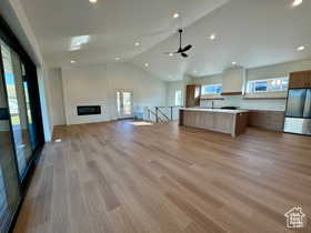 Unfurnished living room featuring lofted ceiling, a fireplace, ceiling fan, and light wood-type flooring