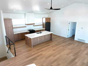 Kitchen featuring sink, light hardwood / wood-style flooring, ceiling fan, black refrigerator, and an island with sink