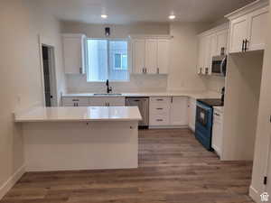 Kitchen with appliances with stainless steel finishes, sink, white cabinets, and kitchen peninsula