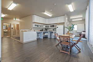 Kitchen featuring white cabinetry, a textured ceiling, white refrigerator, dark hardwood / wood-style flooring, and kitchen peninsula