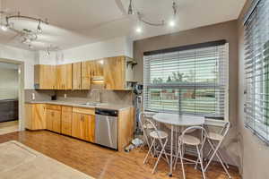 Kitchen featuring sink, backsplash, stainless steel dishwasher, and light hardwood / wood-style floors