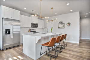 Kitchen with sink, an island with sink, white cabinets, and appliances with stainless steel finishes