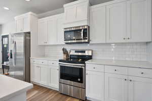 Kitchen with white cabinetry, decorative backsplash, wood-type flooring, and stainless steel appliances