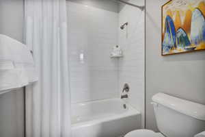 Bathroom featuring toilet and shower / bathtub combination with curtain