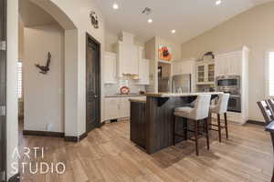 Kitchen featuring a breakfast bar, granite countertopss, an island with sink, stainless steel appliances, and white cabinets