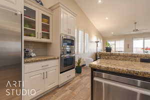 Kitchen with stainless steel appliances, granite  countertops, built-oven, vaulted ceiling, and white cabinets