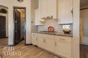 Kitchen with white cabinetry, stainless steel gas stovetop, wood look tile floors, and granite counters