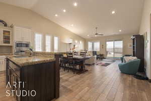 Great room with white cabinetry in kitchen, stainless steel appliances, granite countertops, and light wood look tile floors.