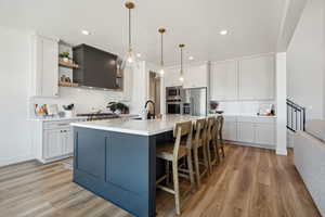 Kitchen featuring pendant lighting, sink, white cabinetry, stainless steel appliances, and a center island with sink