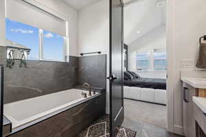 Bathroom featuring tiled tub, vanity, vaulted ceiling, and a healthy amount of sunlight