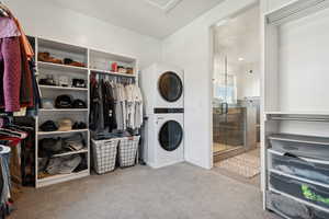 Laundry area with light carpet, a chandelier, and stacked washing maching and dryer