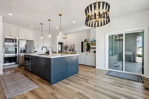 Kitchen with pendant lighting, sink, white cabinets, stainless steel appliances, and a center island with sink