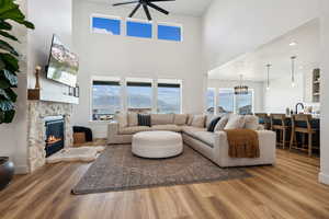 Living room with a stone fireplace, sink, hardwood / wood-style flooring, ceiling fan with notable chandelier, and a high ceiling