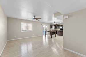 Living room featuring ceiling fan with notable chandelier, light hardwood / wood-style flooring, and a textured ceiling