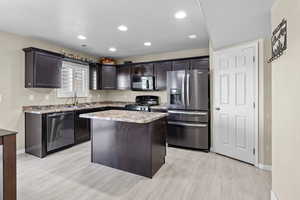 Kitchen with sink, appliances with stainless steel finishes, dark brown cabinets, a center island, and light hardwood / wood-style floors