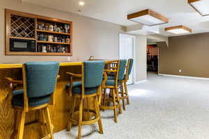 Bar featuring carpet floors, black microwave, and a textured ceiling