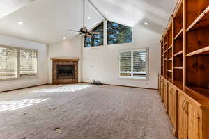 Unfurnished living room with light colored carpet, high vaulted ceiling, a textured ceiling, ceiling fan, and a fireplace