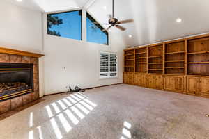 Unfurnished living room featuring ceiling fan, light colored carpet, high vaulted ceiling, and a tile fireplace