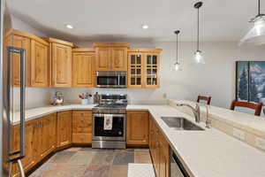 Kitchen featuring a kitchen bar, appliances with stainless steel finishes, decorative light fixtures, and sink