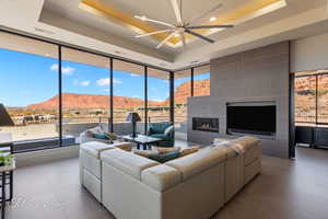 Living room with a tray ceiling, a tile fireplace, and ceiling fan