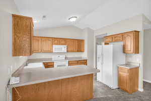 Kitchen with vaulted ceiling, sink, white appliances, and kitchen peninsula