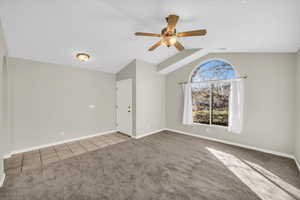 Empty room with vaulted ceiling, light colored carpet, and ceiling fan