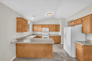 Kitchen with lofted ceiling, sink, white appliances, and kitchen peninsula