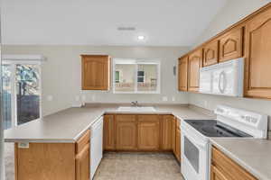 Kitchen with white appliances, lofted ceiling, kitchen peninsula, and sink