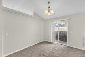 Carpeted empty room featuring lofted ceiling and a notable chandelier