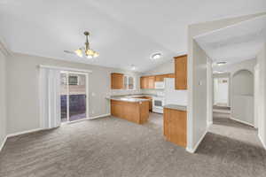 Kitchen featuring decorative light fixtures, light colored carpet, a notable chandelier, kitchen peninsula, and white appliances