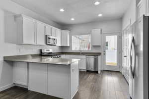 Kitchen with sink, white cabinetry, dark hardwood / wood-style flooring, kitchen peninsula, and stainless steel appliances