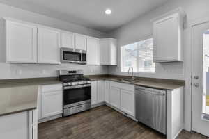 Kitchen with appliances with stainless steel finishes, dark hardwood / wood-style flooring, sink, and white cabinets