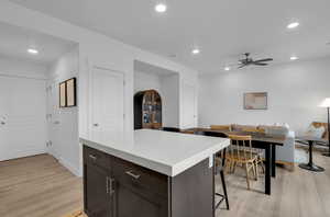 Kitchen with a breakfast bar, a center island, ceiling fan, dark brown cabinets, and light wood-type flooring