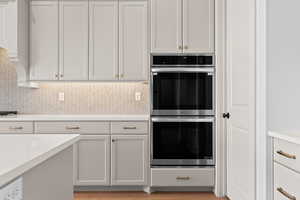 Kitchen featuring white cabinetry, stainless steel double oven, and decorative backsplash