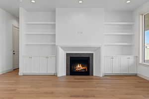 Unfurnished living room featuring built in shelves and light hardwood / wood-style flooring