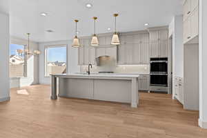 Kitchen featuring gray cabinetry, hanging light fixtures, backsplash, stainless steel double oven, and light wood-type flooring