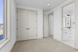 Unfurnished bedroom featuring connected bathroom, sink, light colored carpet, and a closet