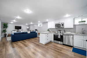 Kitchen with sink, wood-type flooring, kitchen peninsula, stainless steel appliances, and white cabinets