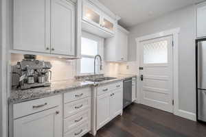 Kitchen with dark wood-type flooring, sink, stainless steel appliances, decorative backsplash, and white cabinets