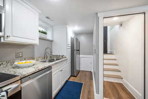 Kitchen with dark wood-type flooring, sink, stainless steel appliances, light stone countertops, and white cabinets