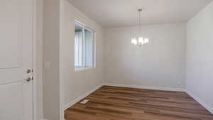 Unfurnished dining area with dark wood-type flooring, baseboards, and a chandelier