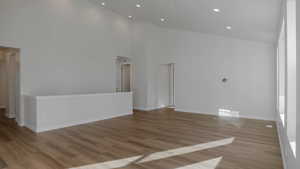 Unfurnished room with a high ceiling, recessed lighting, wood finished floors, and baseboards