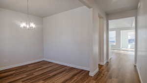 Unfurnished room featuring an inviting chandelier, baseboards, and wood finished floors