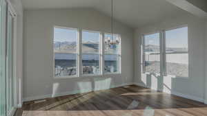 Unfurnished dining area featuring vaulted ceiling, wood finished floors, baseboards, and a chandelier