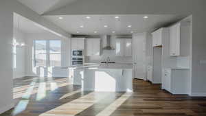 Kitchen with dark wood-type flooring, oven, wall chimney range hood, built in microwave, and white cabinetry
