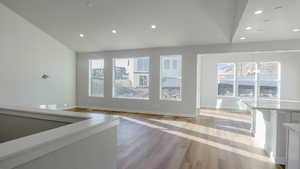 Unfurnished living room featuring baseboards, an inviting chandelier, light wood-style flooring, lofted ceiling, and recessed lighting