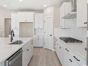 Kitchen with wall chimney range hood, stainless steel appliances, sink, and light stone countertops