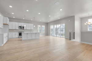 Kitchen with white cabinetry, stainless steel appliances, decorative light fixtures, and a center island with sink