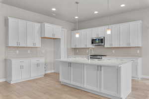 Kitchen featuring an island with sink, pendant lighting, and white cabinets