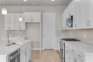 Kitchen featuring sink, white cabinetry, stainless steel appliances, light hardwood / wood-style floors, and decorative light fixtures